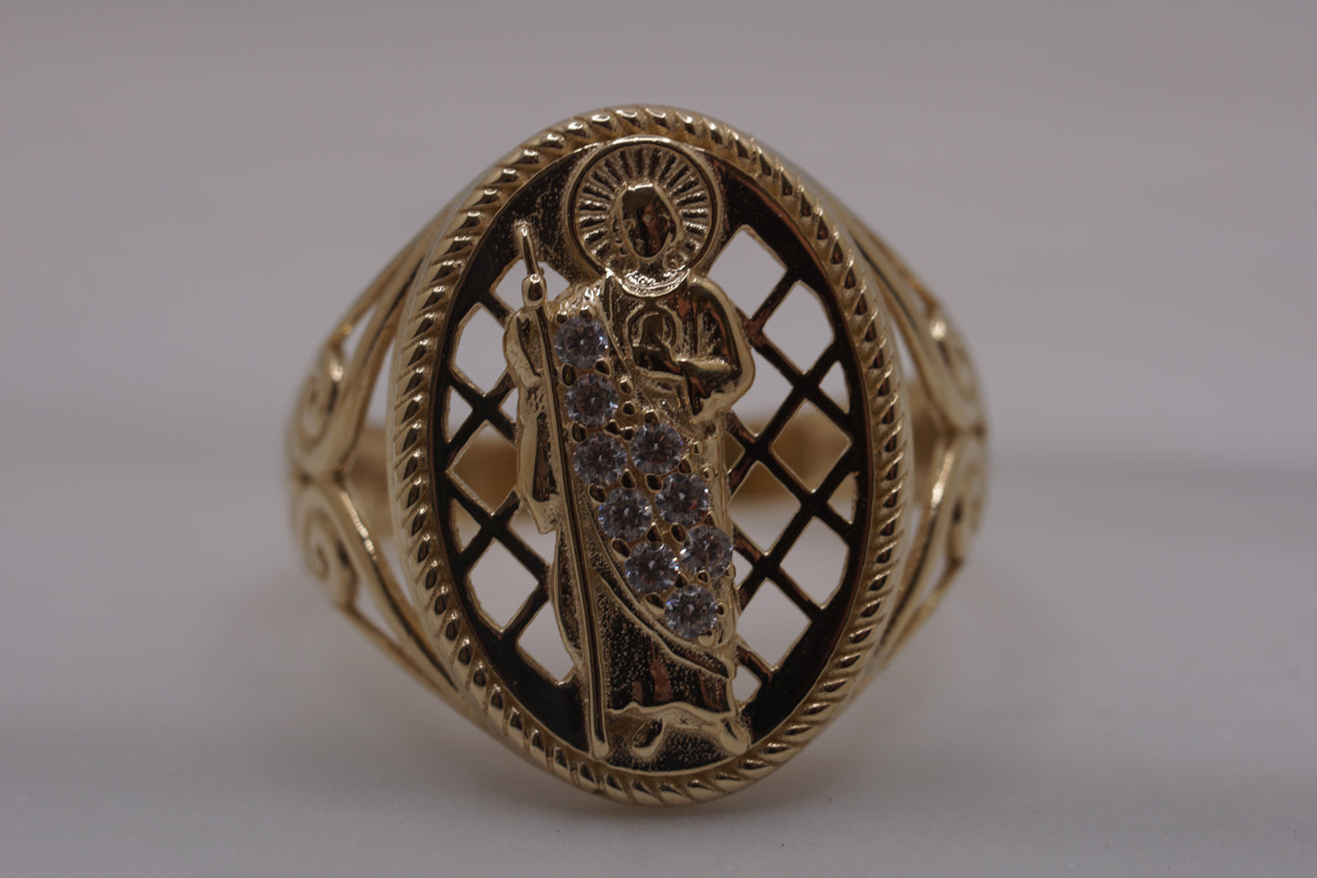 Close-up of 14K yellow gold San Judas ring with detailed designs on the bands and white CZ stones on the face.