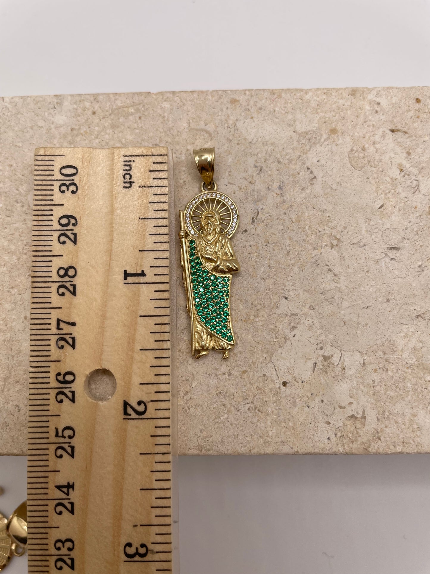 14K yellow gold San Judas pendant with CZ halo and green CZ body, shown next to a ruler to display dimensions (approximately 1.5 inches)