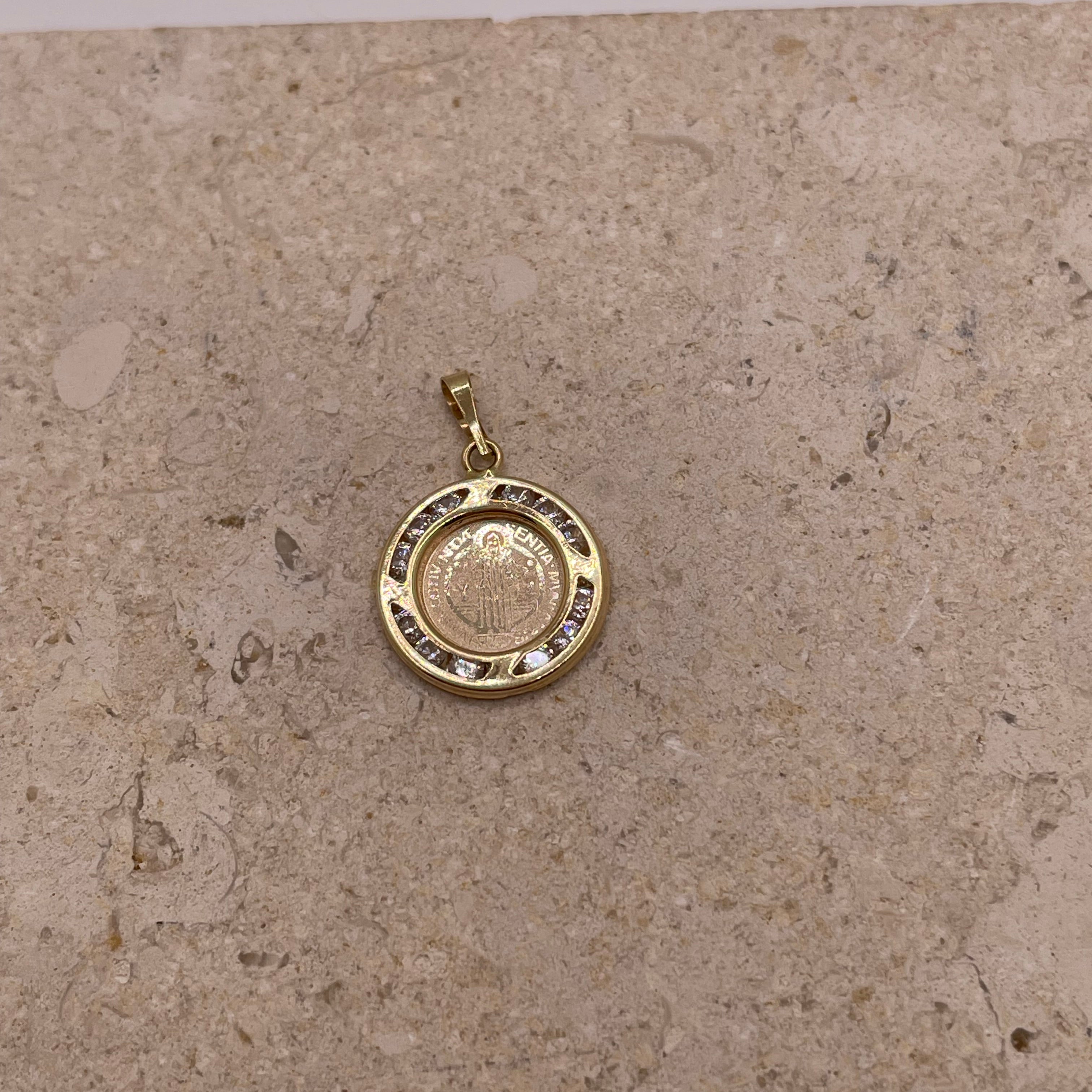 A close-up image of the 14k gold San Benito pendant featuring the detailed design of the Saint Benedict medal at the center, surrounded by a sparkling border of cubic zirconia stones.