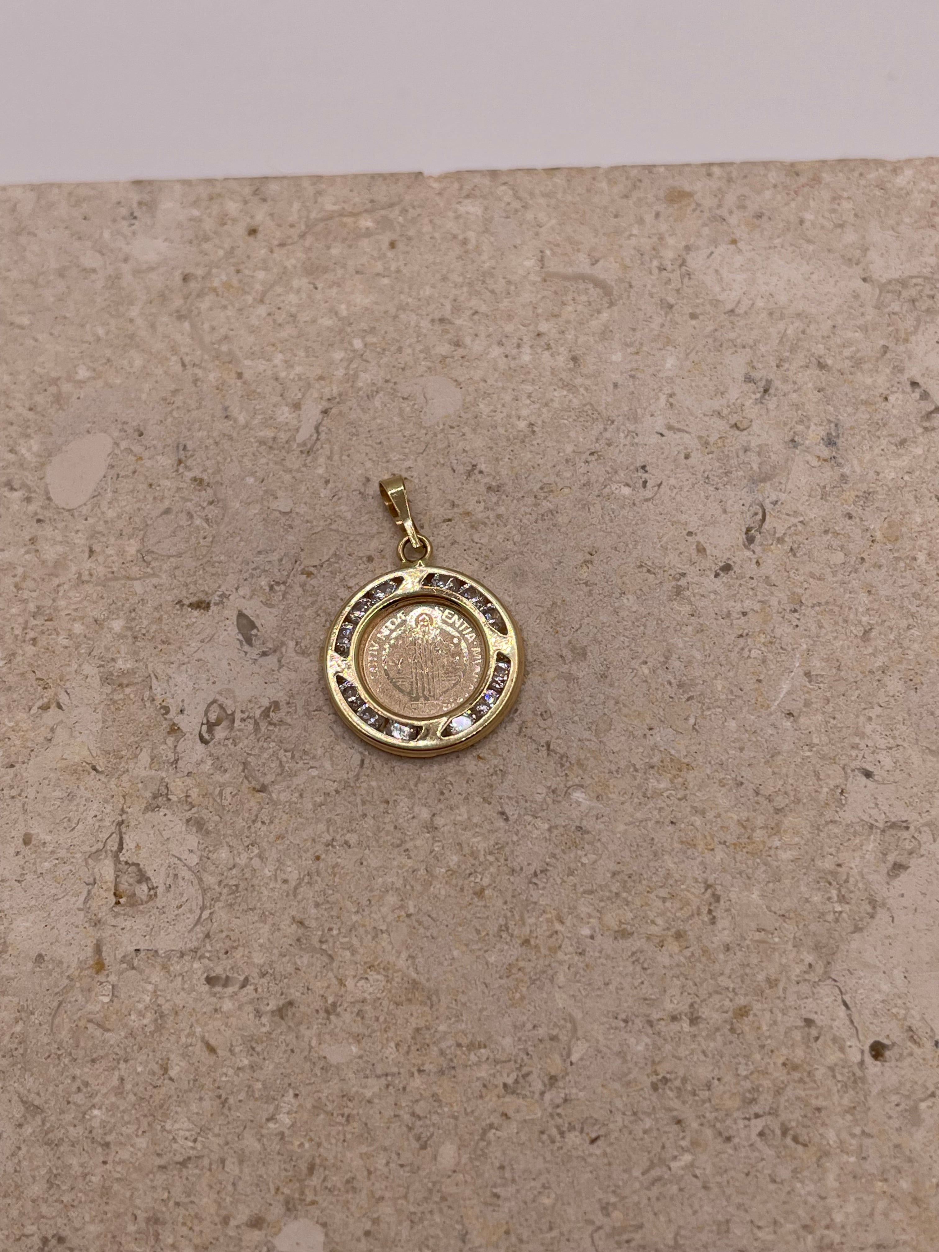 A close-up image of the 14k gold San Benito pendant featuring the detailed design of the Saint Benedict medal at the center, surrounded by a sparkling border of cubic zirconia stones.